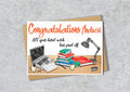 Greeting card with 'Congratulations Andrew' text and a illustration of a desk with books, laptop, and lamp.