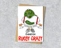 Greeting card with rugby ball and green cap illustration with red "Rugby Crazy" a personalised name and favourite team in the scarf.